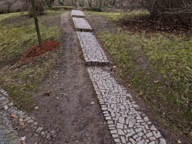 Yaya yolunun yeşil çimenli gri renginde, dar bir kısayoldaki merdivenlerle ıslak, eğimli yolu olan bir parkın etrafında düzensiz yontulmuş taşlardan oluşan granit kaldırımlar.