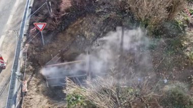 Derin zırhlı kuyudaki boruları sıcak suyla ya da buharla onarmak sisli ya da tozlu bir madeni andırıyor. Giriş ve bant engeline karşı korunmak için geçici bina çiti ile sınırlandırılmış.