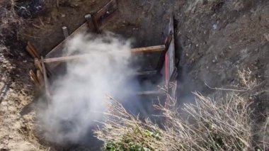 Derin zırhlı kuyudaki boruları sıcak suyla ya da buharla onarmak sisli ya da tozlu bir madeni andırıyor. Giriş ve bant engeline karşı korunmak için geçici bina çiti ile sınırlandırılmış.
