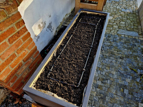corner of the family garden with several beds bordered by boards. there is compacted sand around and the paving irregularly jaggedly rises into the mortar. flowering beds with annuals