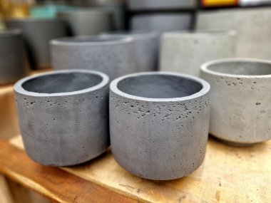 Gri beton saksılar, satılık bir depoda dizilmiş. Üst üste yığılmış plastik beyaz tuğla küvetleri. Fabrika ve masa için ucuz tasarım konteynırları üretimi