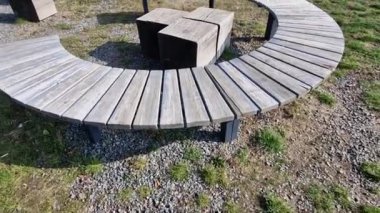 Parkta üç yuvarlak bank var. Izgara tam oturmanın ortasında. Büyük ahşap panelli hilal bir pergola altındaki bir çayırda. Büyük ahşap bloklar