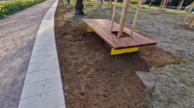 Parkı gören yükseltilmiş teras, tahta panelli ve dikdörtgen banklı beton uzun bir saksı. Şehrin sokaktaki ve meydandaki gezinti alanlarından biri.