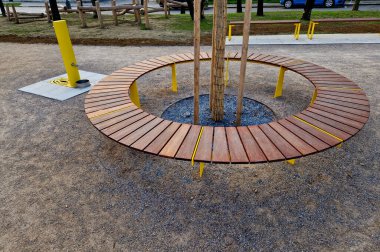 Tahtadan yapılmış yuvarlak bank bir ağacı çevrelemiş, ahşap panellerle oturuyormuş. Metal çerçeve Ağacın etrafındaki tahtalardan oluşan bölümler. Köklerdeki havalandırma ve sulama şebekeleri