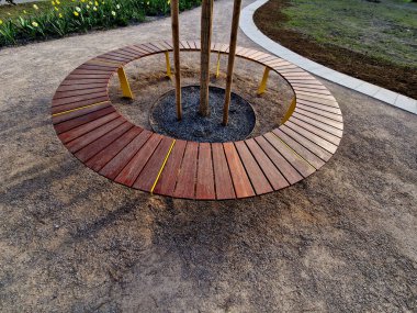 Tahtadan yapılmış yuvarlak bank bir ağacı çevrelemiş, ahşap panellerle oturuyormuş. Metal çerçeve Ağacın etrafındaki tahtalardan oluşan bölümler. Köklerdeki havalandırma ve sulama şebekeleri