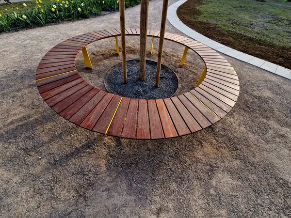 Tahtadan yapılmış yuvarlak bank bir ağacı çevrelemiş, ahşap panellerle oturuyormuş. Metal çerçeve Ağacın etrafındaki tahtalardan oluşan bölümler. Köklerdeki havalandırma ve sulama şebekeleri