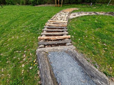 Tactile path for bare feet awakens the senses and uneven endings on the feet alternating different materials wood stone gravel sand bark in a park environment, sensoric, red, bent, curved, log