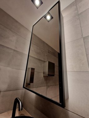 Etrafında lamba olan dairesel bir ayna olan ultradeniz mavisi kaplı mavi fayanslar. Sonra arka ışıklandırması olan gri beton alçıdan basit bir ayna, karanlık bir kulüp atmosferi.