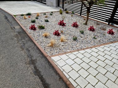 ornamental flower bed with perennial pine and gray granite boulders, mulched bark and pebbles in an urban setting near the parking lot shopping center. clipart