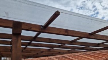 Ahşap pergola ve pleksiglass çatılı teras. Sarmaşıklar geriliyor, kirişlerin altında sürünüyorlar. Bahçe ya da park. Alkolsüz duvar şarabı bölgesinde oturuyor. Kırsal restoran Fransa, kiriş, küre, lamba