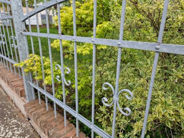 Sahte arsa, salkım salkımı ve süs çalı ile kaplanmış. Galvanize metal, tuğla sütunlar. Tarihi yerleşim yerinin çiti.