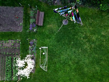 Bahçede sebze bahçesi ve futbol golleri olan bir elbise rafı. bahar çiçekli çalılar, tarlalar ve çatı