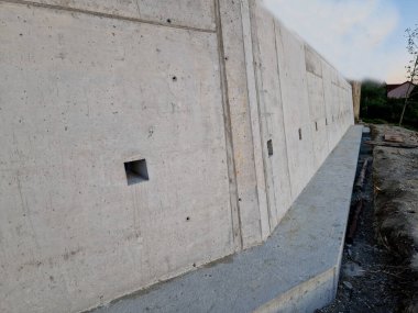 long straight supporting wall of cast cement mixer formwork. behind wall is soil that is brought out through the wall by drainage pipes. sewer pipe drain in line. construction site, white, field