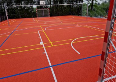 Okuldaki top oyunları için çok işlevli açık hava oyun alanı. Yeşil yapay çim, çizgileri olan plastik bir halıdan. Basketbol potaları ve futbol golleri. Ağı ve korkulukları çevreleyen, 