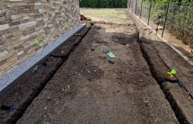 Sulama yeri kazar ve hortumları suyla doldurur. Fıskiyeler bayraklarla işaretlenir. Hendek kazıcı çabucak toprağı kazar.