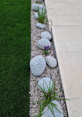 a narrow flower bed along the driveway to the house made of light beige ceramic tiles. boulders softened by water with pebbles, a bed filled with pebbles clipart
