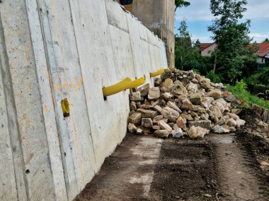 long straight supporting wall of cast cement mixer formwork. behind wall is soil that is brought out through the wall by drainage pipes. sewer pipe drain in line. construction site, white, field