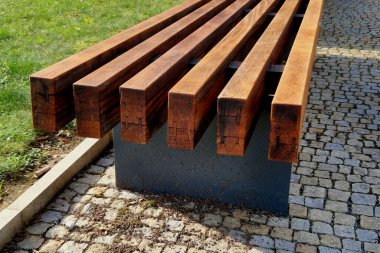 Parkı gören yükseltilmiş teras, tahta panelli ve dikdörtgen banklı beton uzun bir saksı. Şehrin cadde ve meydanındaki gezinti alanlarından biri.