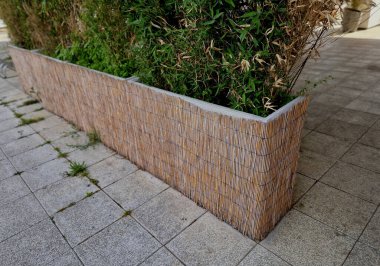 Restoranın ön bahçesinde, çiçek saksıları birkaç iple bağlanır ve açık kafede oturmak için bir çit sağlar. Kamış hasırıyla kaplı bir saksı.