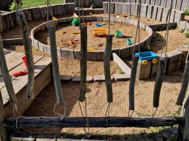 Oturma ve çıplak ayakla yürüyebileceğin dokunsal bir yürüyüş yolu. Ortada bir kum havuzu var. Ahşap çayırlardan ve askıya alınmış ahşap süvarilerden oluşan bir çocuk parkı.