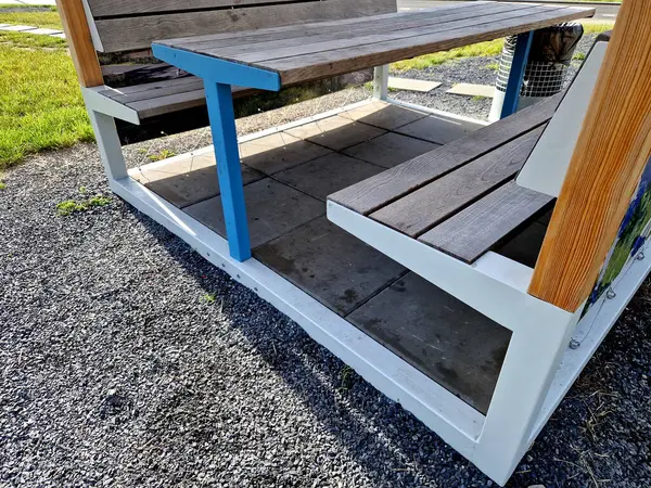 stock image a pergola made of beams covered with tarpaulins and tied with eyelets as an advertising banner to the steel cable structure. shading fabric of yellow and beige slats protects  camping bench , table