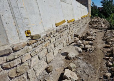 long straight supporting wall of cast cement mixer formwork. behind wall is soil that is brought out through the wall by drainage pipes. sewer pipe drain in line. construction site, white, field