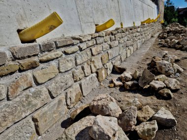 long straight supporting wall of cast cement mixer formwork. behind wall is soil that is brought out through the wall by drainage pipes. sewer pipe drain in line. construction site, white, field