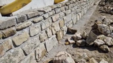 long straight supporting wall of cast cement mixer formwork. behind wall is soil that is brought out through the wall by drainage pipes. sewer pipe drain in line. construction site, white, field