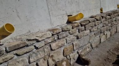 long straight supporting wall of cast cement mixer formwork. behind wall is soil that is brought out through the wall by drainage pipes. sewer pipe drain in line. construction site, white, field