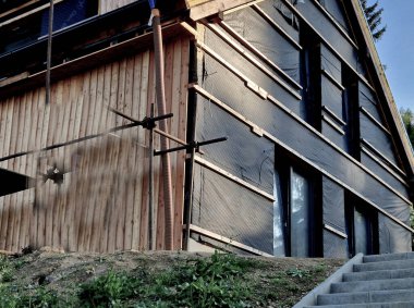 Binanın etrafına galvanize borulardan yapılmış iskeleler kuruluyor, ön cephelerin tahtalardan yapıldığı ve asılmış yapının yalıtımının yapıldığı bina. Ahşap tarla paneli