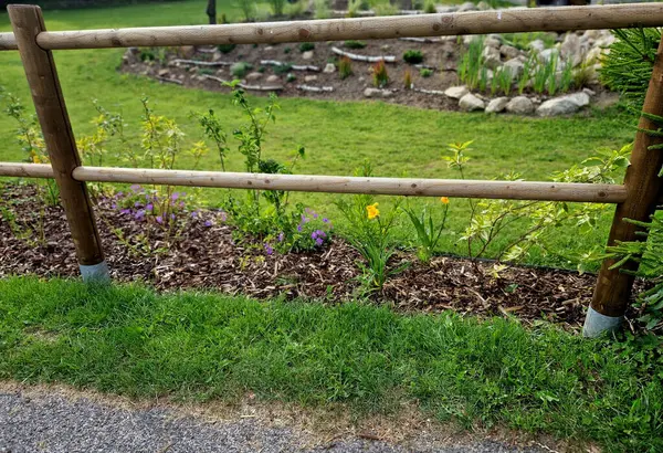 Stock image rural fencing made of hewn stove posts style enclosure in the mountains. a bed mulched with bark and perennial blue flowers along the edge