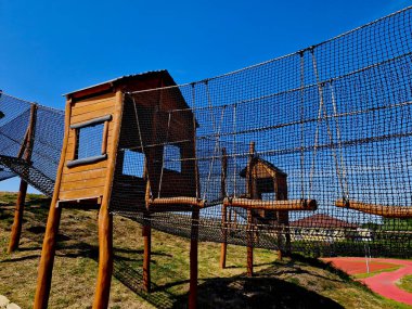 netted tunnel made of ropes. visitor child, crawling through the labyrinth. stainless steel slide. urban parl mebo school yard wooden attraction castle