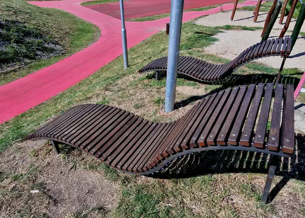 design bench in the shape of a wavy line. wooden paneling on a metal galvanized frame. The bench is atypical to order in a city park for young people and unusual sitting and lying