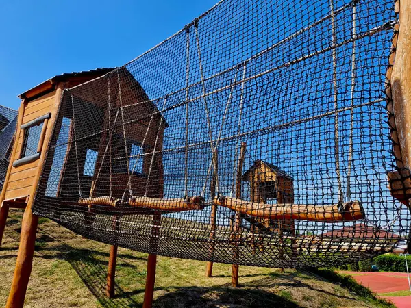 netted tunnel made of ropes. visitor child, crawling through the labyrinth. stainless steel slide. urban parl mebo school yard wooden attraction castle