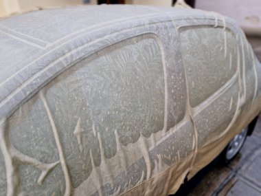 Şehvetli ıslak kumaş arabanın metal levhalarının kıvrımlarına sarılıyor. Araba toplantısı için erotik bayan ıslak gömlek. Örtü, boyayı güneşten korumak için..