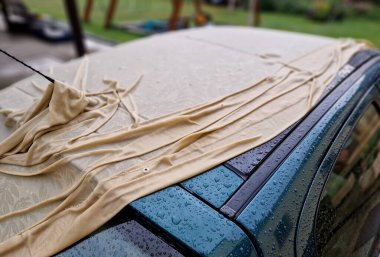 Şehvetli ıslak kumaş arabanın metal levhalarının kıvrımlarına sarılıyor. Araba toplantısı için erotik bayan ıslak gömlek. Örtü, boyayı güneşten korumak için..