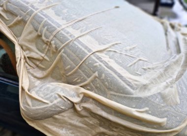 Şehvetli ıslak kumaş arabanın metal levhalarının kıvrımlarına sarılıyor. Araba toplantısı için erotik bayan ıslak gömlek. Örtü, boyayı güneşten korumak için..