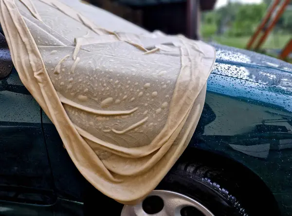 Şehvetli ıslak kumaş arabanın metal levhalarının kıvrımlarına sarılıyor. Araba toplantısı için erotik bayan ıslak gömlek. Örtü, boyayı güneşten korumak için..