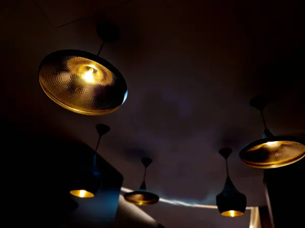 stock image designer lights made of sheet metal hang from the ceiling. inside they are golden or bronze yellow. in the kitchen or hallway in a group of different shapes