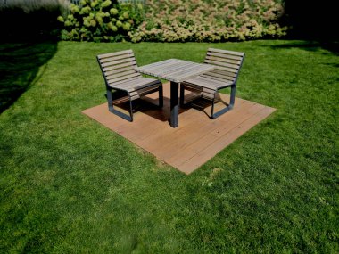 Park mobilyaları satranç masası ve açık metalden yapılmış dört kişi için sandalyeler ve geri tepme parlak kayalık arazili ahşap kirişler çakıl çimenleri yeşil akşam güneşi 
