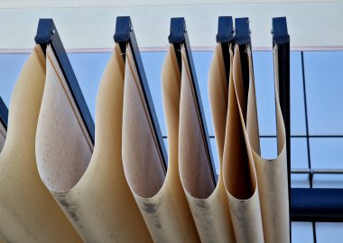 Pergola 'nın dalgalı kumaşı terasa uzanıyor. Lastik kumaş yağmura dayanıklıdır. İndirme uzaktan kumandalı motorlar tarafından sağlanıyor. Cam cepheli bir ofis binası.