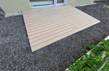 Teraslı bir evde ahşap bir terasın farkına varmak. Küçük bahçelerde, yeni ekilen çimlerin yanı sıra oturmak için bir de plastik tahta ve bir masa bulunur. Fransız penceresi