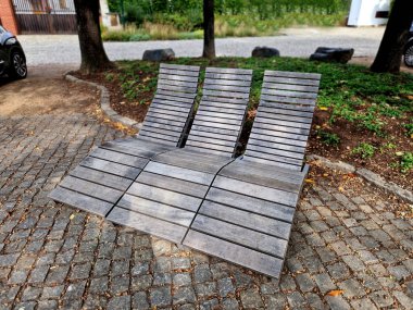 Meydandaki ağaçların altındaki kaldırımda sallanan sandalye. Parktaki tek bir kişi için tropikal ahşaptan yapılmış ahşap sandalyeler. Kahverengi kalaslardan, çatallardan, çelik çerçevelerden ve meşeden yapılma.