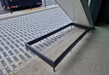 Binanın çıkıntısının altındaki eğimli geçit, yayaların başlarını tavana ya da binanın köşesine çarpmasını engelleyen metal bir çit tarafından tanımlanıyor.