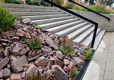 Oturan bir bankla aynı anda parka giden beton merdivenler. Gri çimento pürüzsüz parlak çimento yüzeyi. Granit küpler harman yolu döşüyorlar. Bitkilerle kaplanmış. geniş