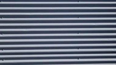 Bina kare panellerle kaplı. Metal kaplama, deniz tarağı desenli. Bükülmüş çarşaf, koyu gri, perçinlenmiş. yatay çizgiler, gölgeler, köşe, çit, alüminyum, çarşaf