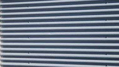 Bina kare panellerle kaplı. Metal kaplama, deniz tarağı desenli. Bükülmüş çarşaf, koyu gri, perçinlenmiş. yatay çizgiler, gölgeler, köşe, çit, alüminyum, çarşaf