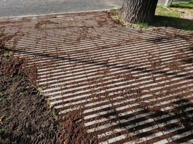 Çizgili boşlukları olan beton gri fayanslar. Çimenler boşluklarda yetişir ve sızma yüzeyi otoparkı ya da kaldırım görevi görür. Ekolojik kaldırım. çakıl döşeme, tırmık, tırmık, tırmık