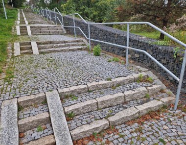 ramp combined with a gray concrete staircase and a handrail specially adapted for wheelchairs. security tasteful solution for entering a city park. sheet metal rails, pram, mother, wheels