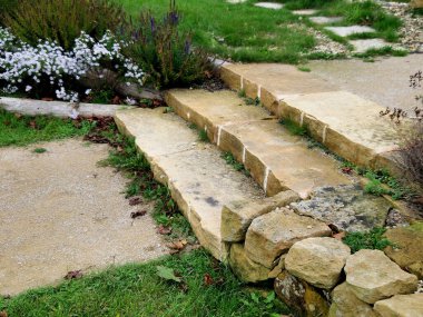 sandstone walls and stones in a flowerbed in a terraced terrain with stairs. flowering rock gardens and stairs with a gravel surface. herb garden clipart